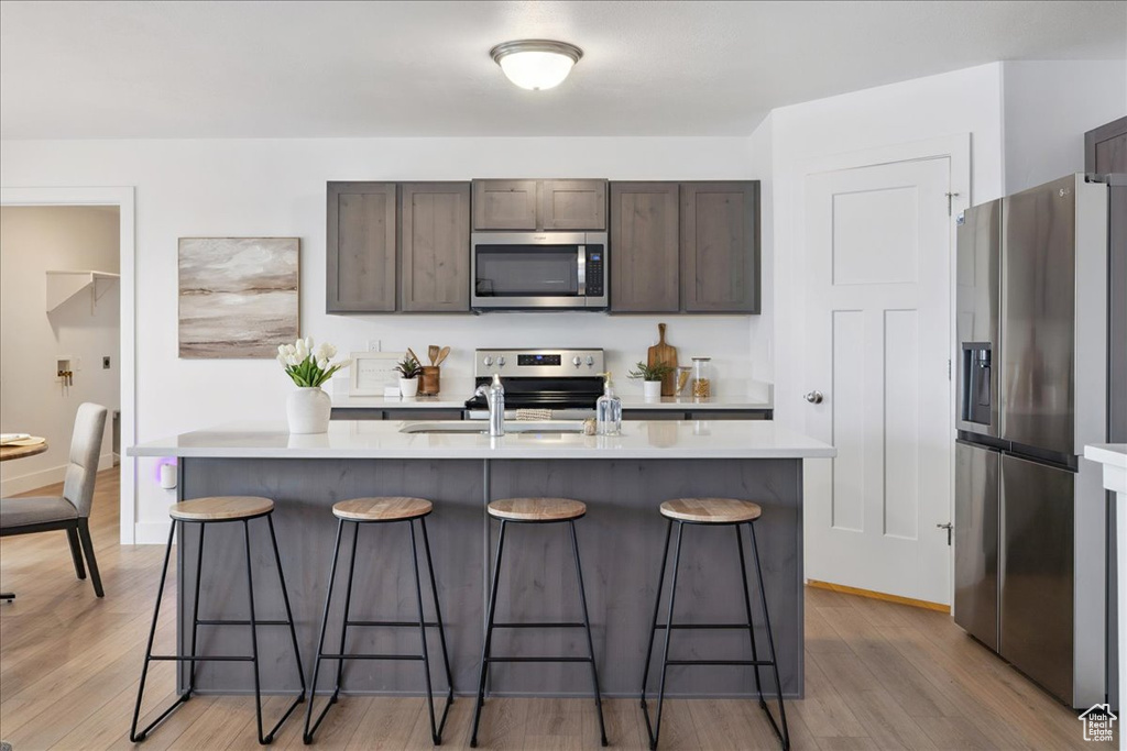 Kitchen with appliances with stainless steel finishes, light countertops, a kitchen bar, and light wood-type flooring