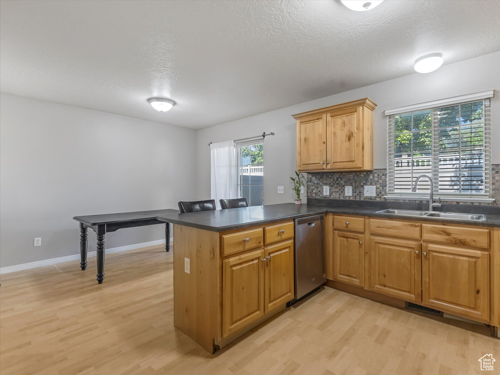 Kitchen with dishwasher, light wood finished floors, dark countertops, a peninsula, and a textured ceiling