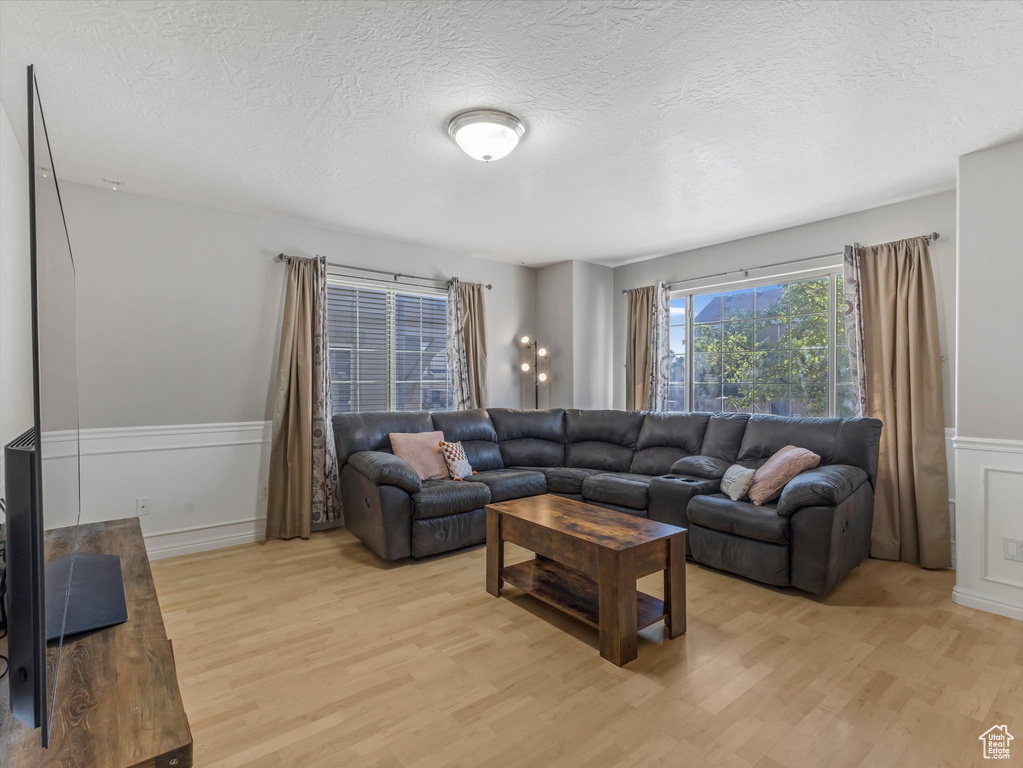 Living area featuring light wood-style flooring, wainscoting, a textured ceiling, and a decorative wall