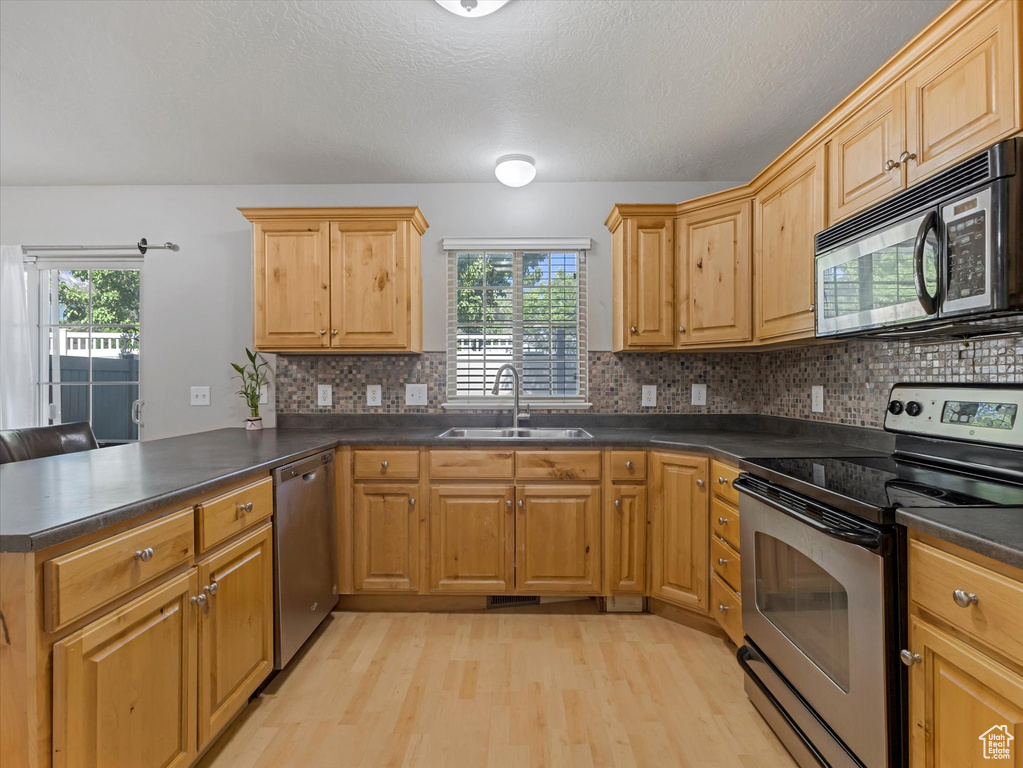 Kitchen with stainless steel appliances, a peninsula, light wood finished floors, dark countertops, and backsplash