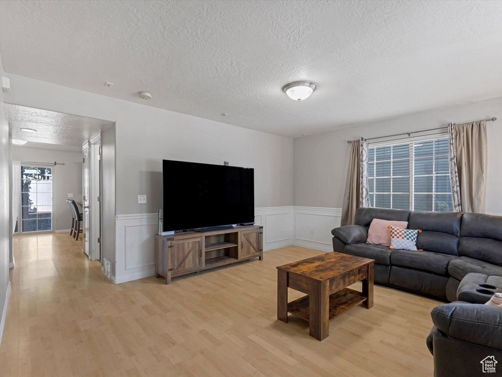 Living area featuring a textured ceiling, light wood-style floors, wainscoting, and a decorative wall