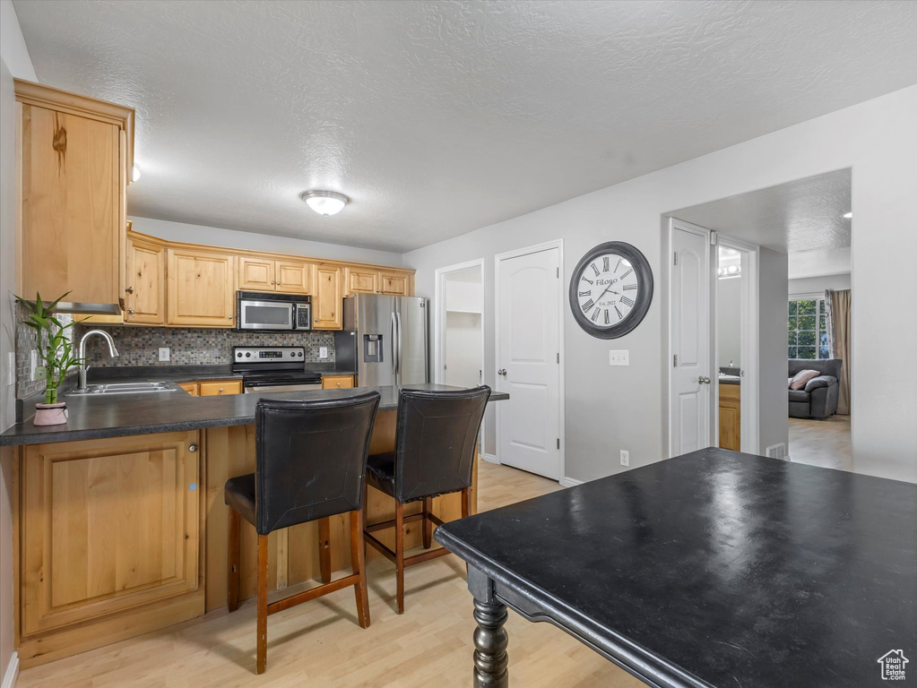 Kitchen with appliances with stainless steel finishes, a peninsula, light wood finished floors, dark countertops, and a textured ceiling