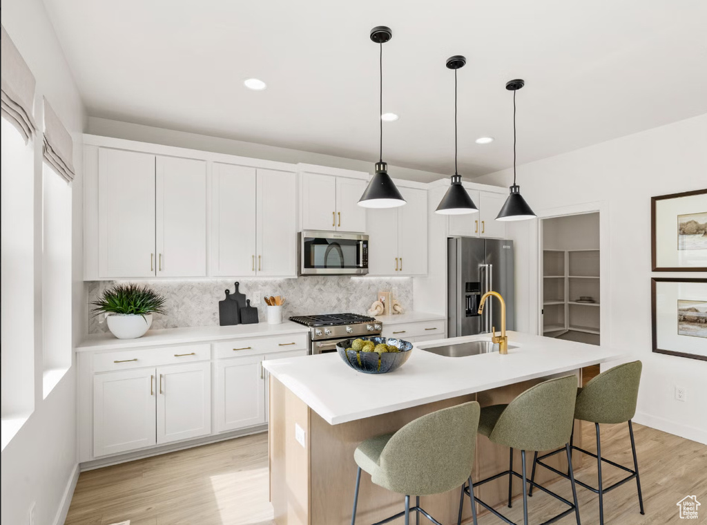 Kitchen featuring appliances with stainless steel finishes, decorative backsplash, a kitchen island with sink, light wood-style flooring, and recessed lighting