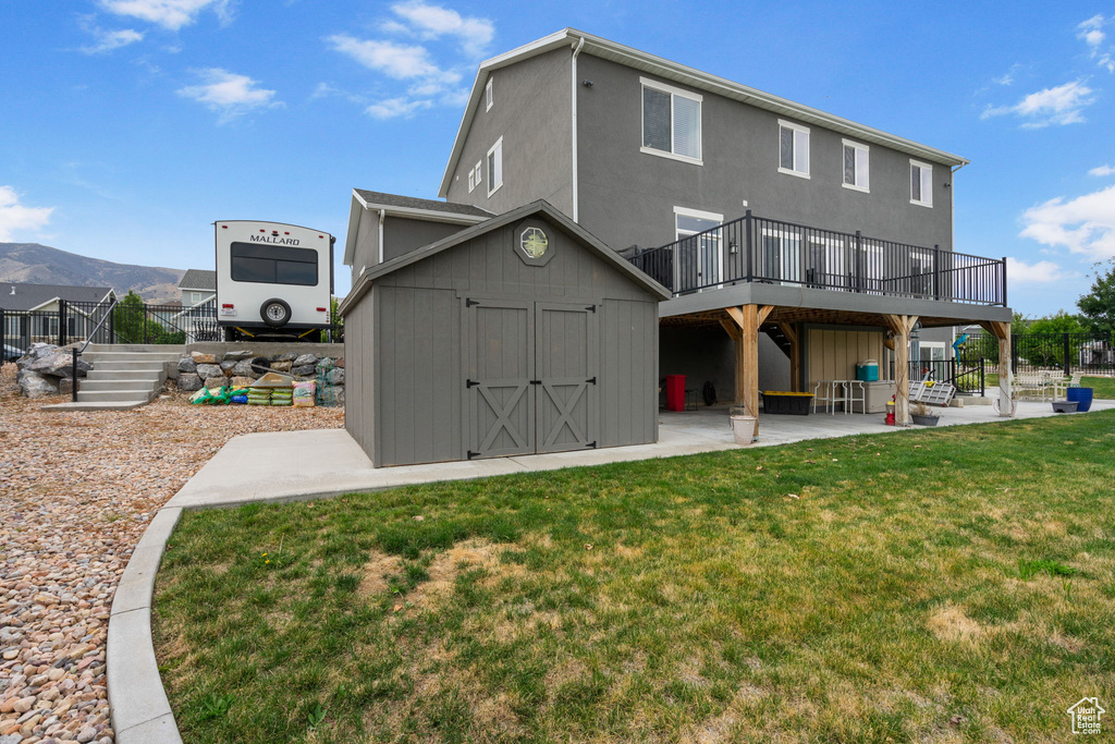 Rear view of property with a storage unit, a yard, a patio area, a deck with mountain view, and stucco siding