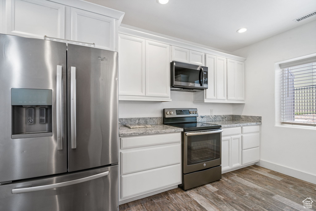 Kitchen featuring stainless steel appliances, white cabinetry, wood finished floors, recessed lighting, and light stone counters