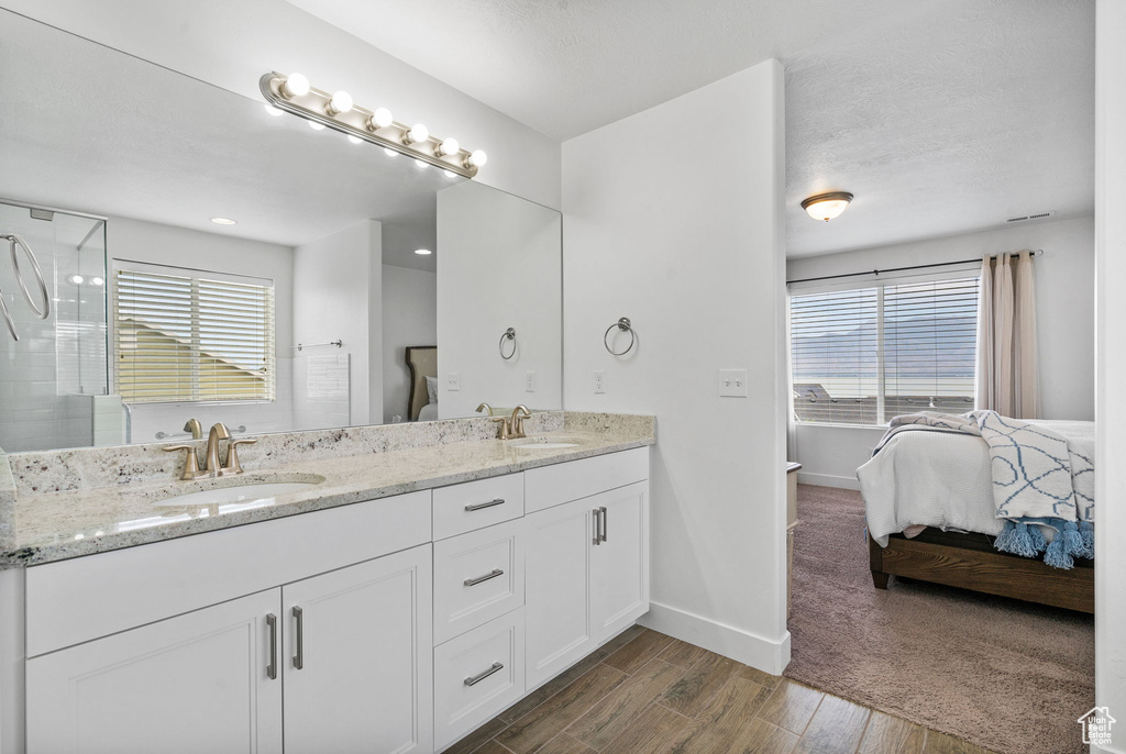 Full bathroom featuring double vanity, ensuite bathroom, healthy amount of natural light, and wood finished floors