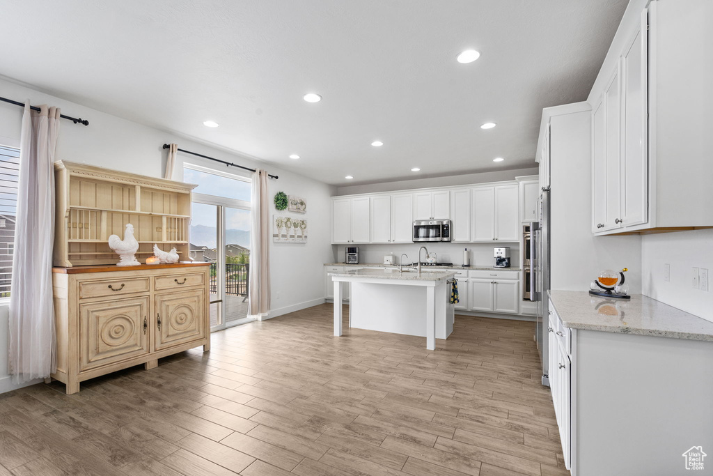 Kitchen featuring a breakfast bar, light wood-style flooring, white cabinets, recessed lighting, and stainless steel microwave