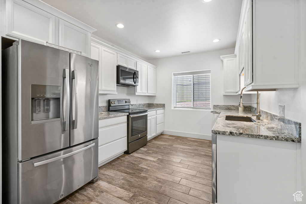 Kitchen with stainless steel appliances, white cabinets, light wood-style flooring, recessed lighting, and light stone counters