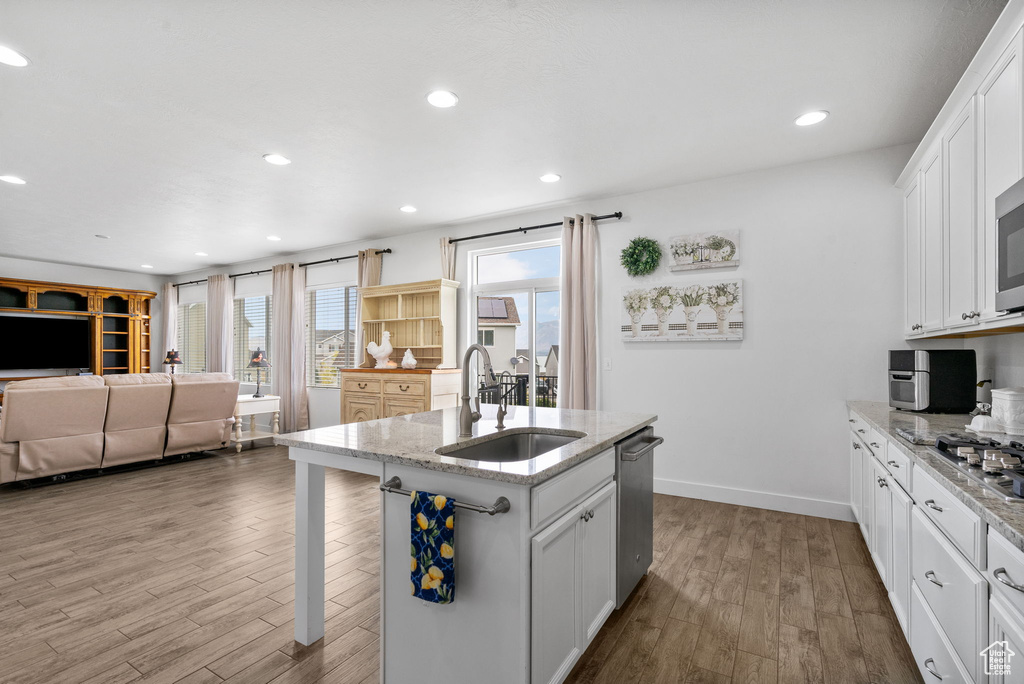Kitchen with wood finished floors, open floor plan, light stone counters, white cabinetry, and a center island with sink