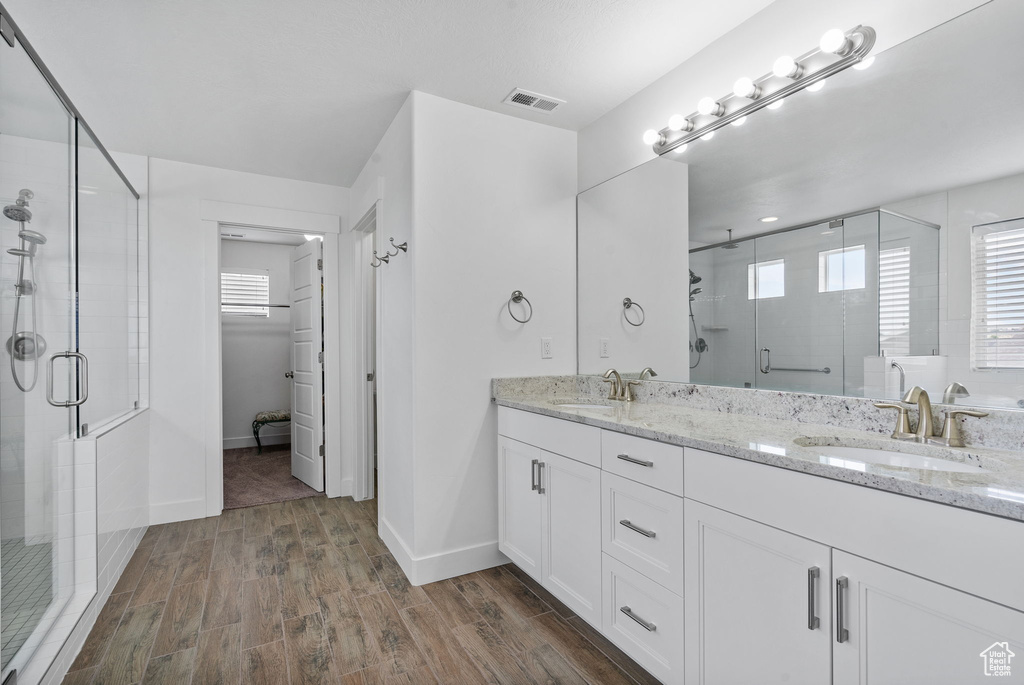 Full bath with a stall shower, wood finished floors, double vanity, and a spacious closet