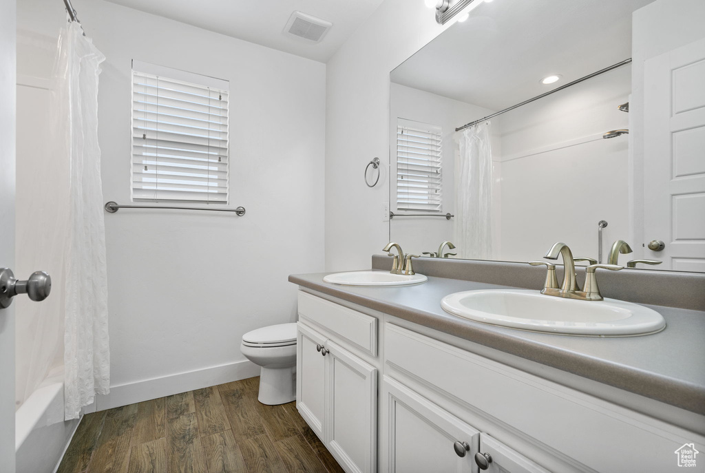Full bathroom featuring double vanity, wood finished floors, and shower / tub combo with curtain