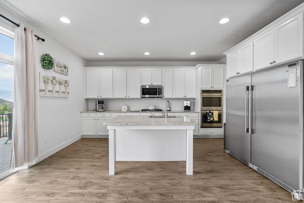 Kitchen with appliances with stainless steel finishes, recessed lighting, an island with sink, white cabinets, and light wood-style floors