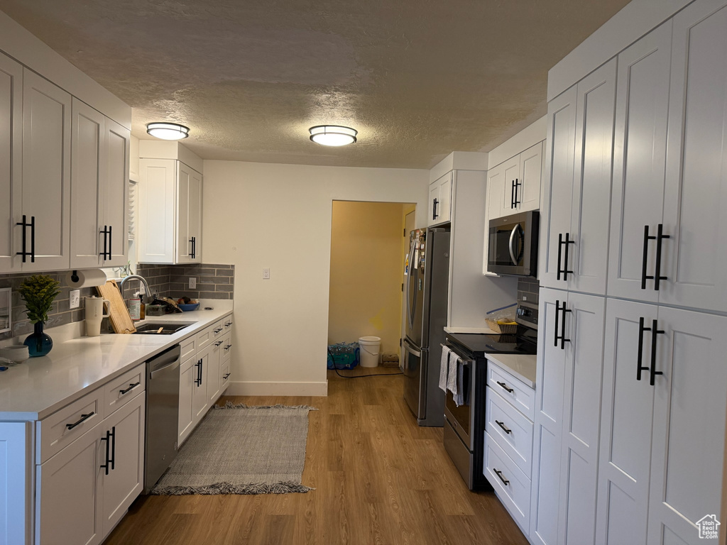 Kitchen featuring stainless steel appliances, backsplash, light countertops, white cabinetry, and wood finished floors