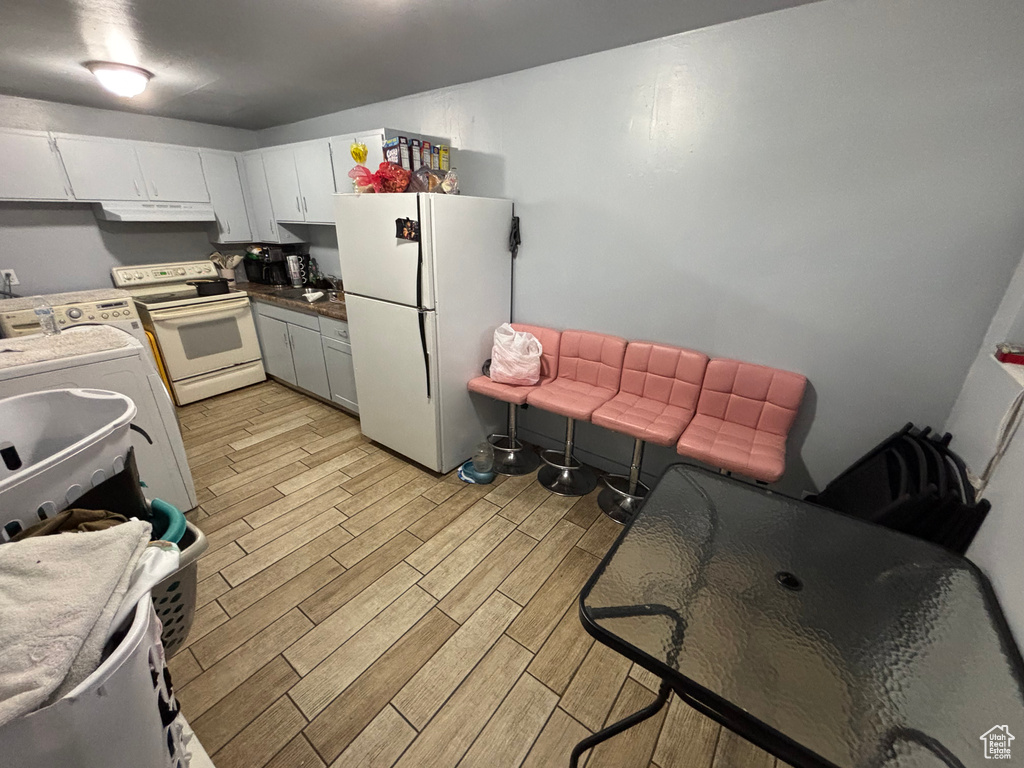 Kitchen featuring white appliances, wood tiled floors, washer / clothes dryer, under cabinet range hood, and white cabinets