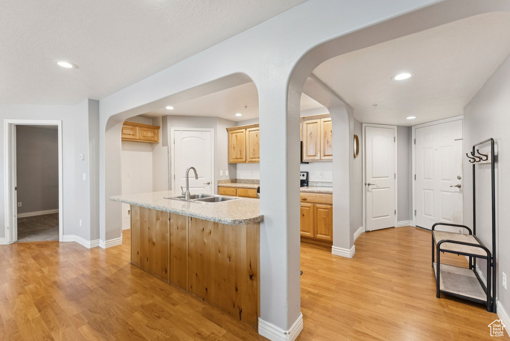 Kitchen featuring arched walkways, light wood-style flooring, recessed lighting, a center island with sink, and light brown cabinetry