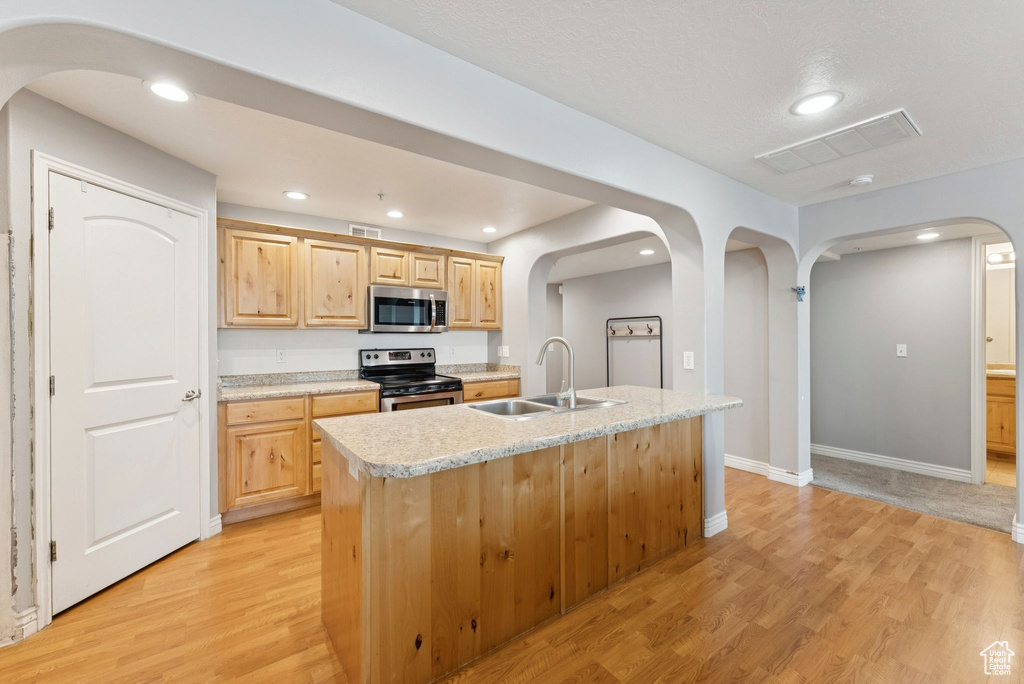 Kitchen featuring arched walkways, light brown cabinets, appliances with stainless steel finishes, light wood-style floors, and recessed lighting