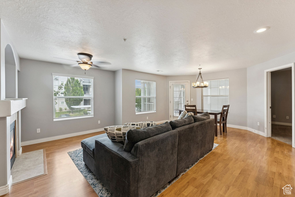 Living area featuring light wood finished floors, a chandelier, a fireplace, and a ceiling fan