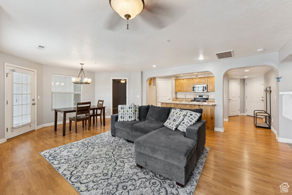 Living room with arched walkways, light wood-style flooring, a chandelier, and a ceiling fan