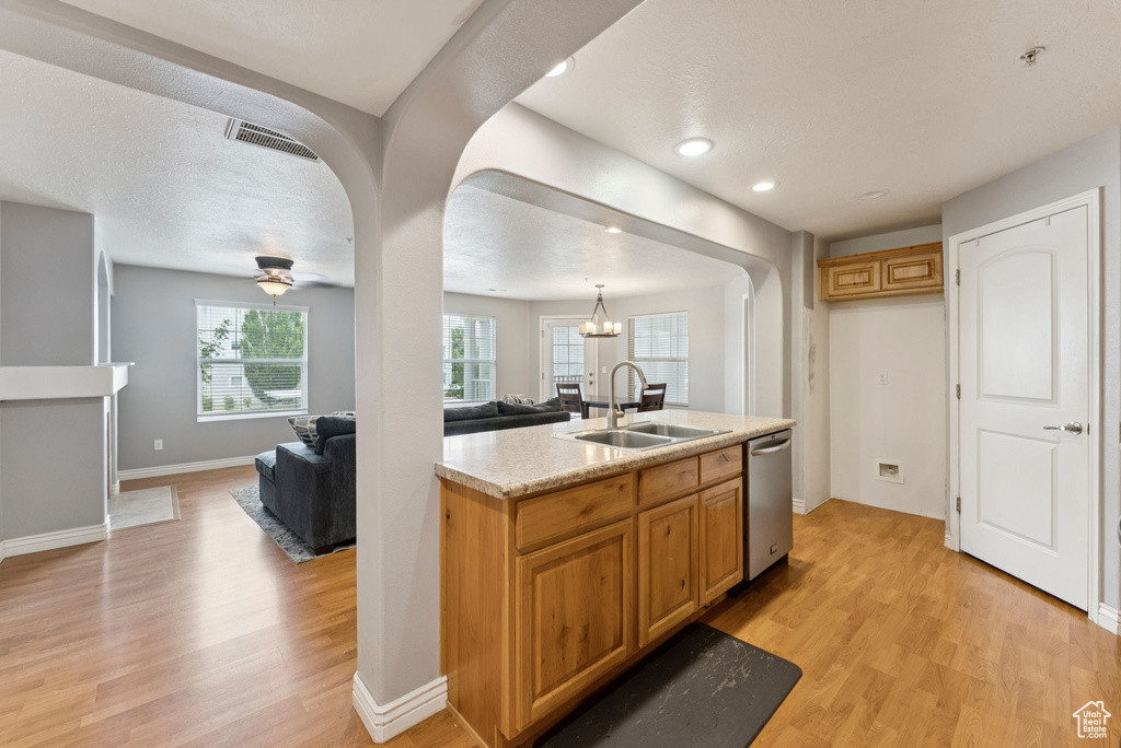 Kitchen with open floor plan, light wood-style floors, a center island with sink, arched walkways, and dishwasher