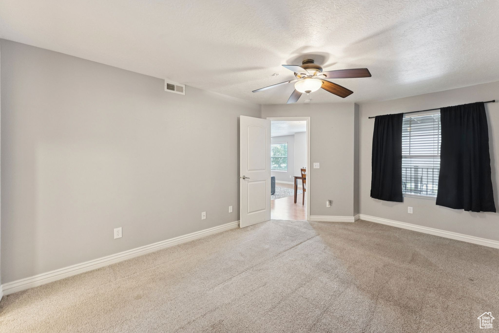 Spare room with ceiling fan, light colored carpet, and a textured ceiling