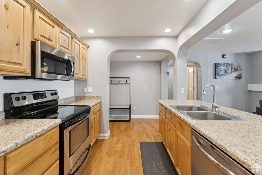 Kitchen featuring appliances with stainless steel finishes, arched walkways, light wood-style floors, light brown cabinetry, and light countertops