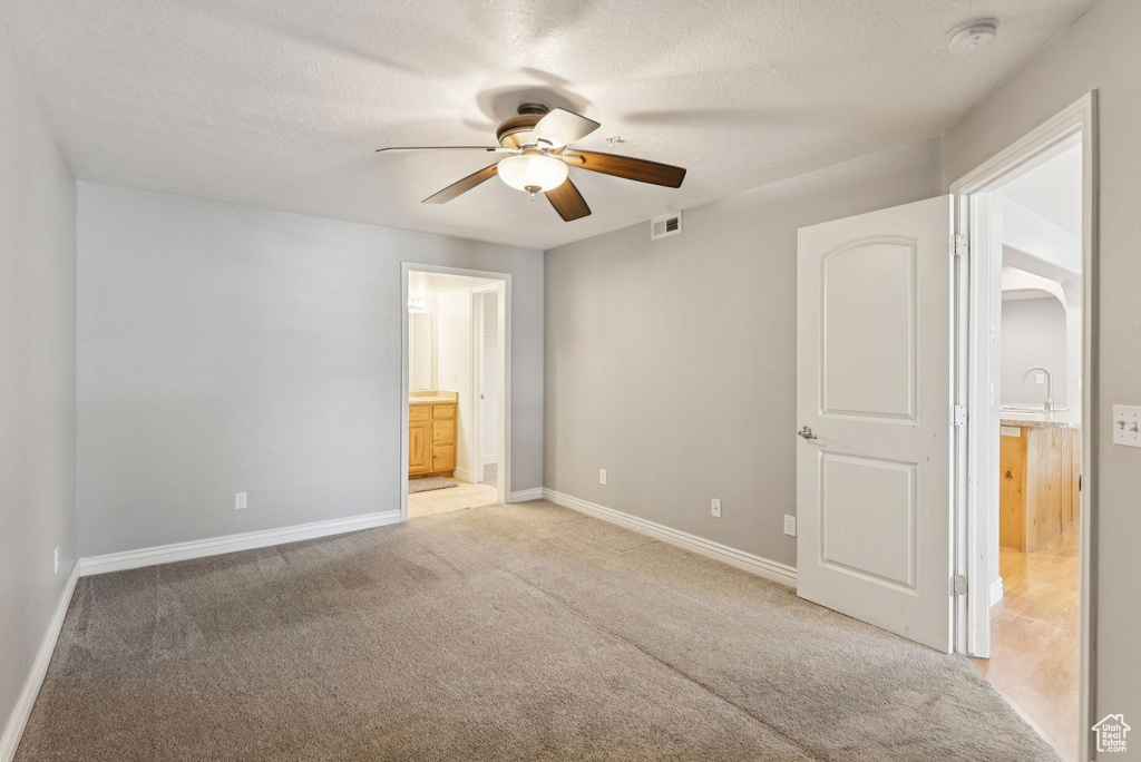 Unfurnished bedroom featuring ensuite bathroom, light colored carpet, arched walkways, a ceiling fan, and a textured ceiling