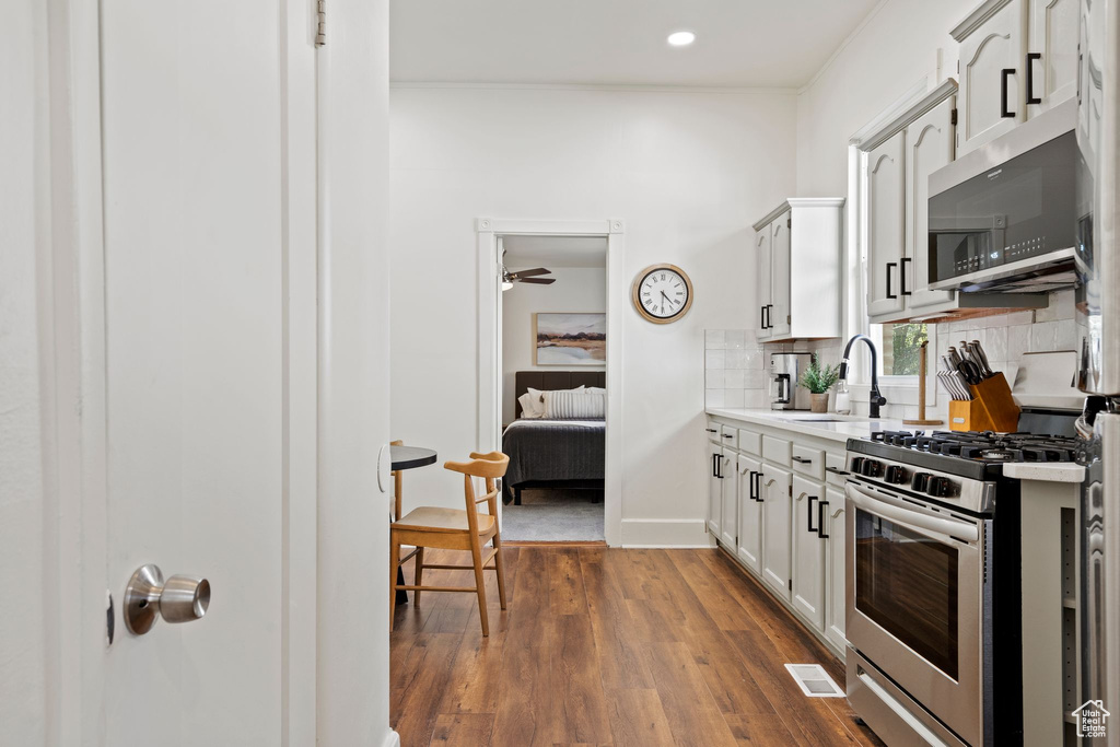 Kitchen featuring stainless steel appliances, tasteful backsplash, light countertops, dark wood-style floors, and white cabinets