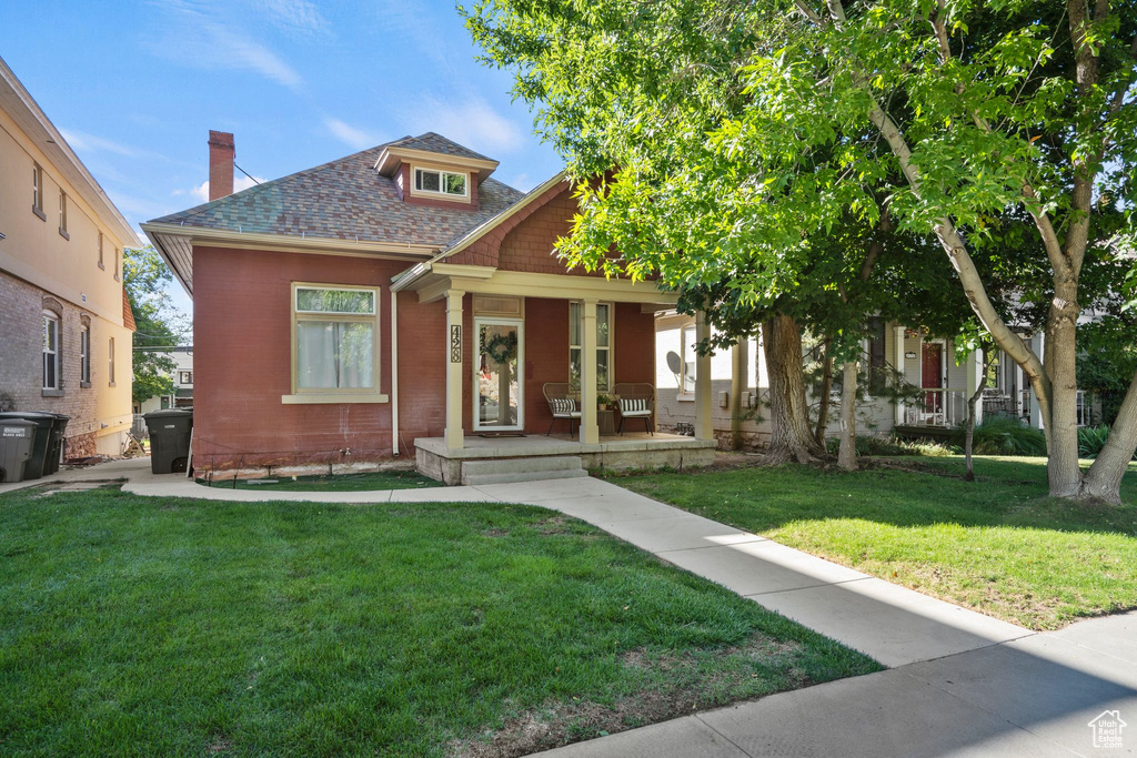 View of front of home featuring covered porch, roof with shingles, a front lawn, and a chimney