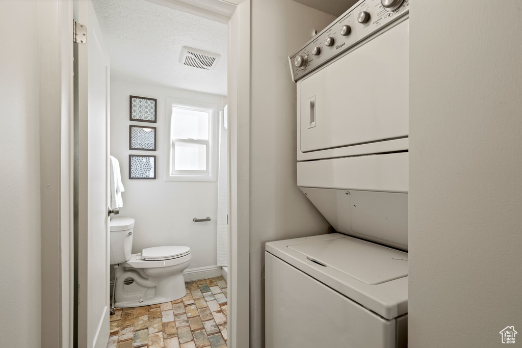 Laundry area with stacked washing machine and dryer and stone finish flooring