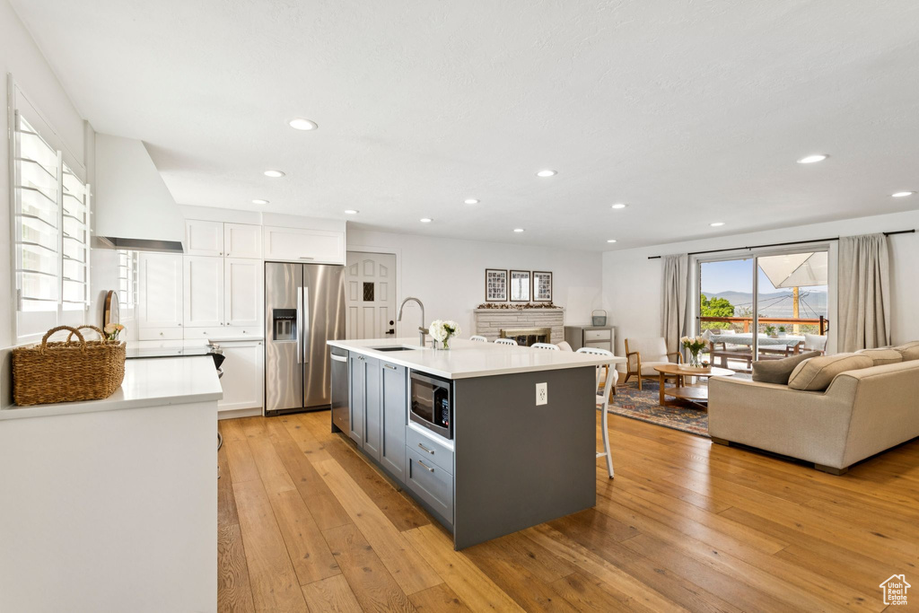 Kitchen with gray cabinets, open floor plan, appliances with stainless steel finishes, light wood-style flooring, and white cabinets