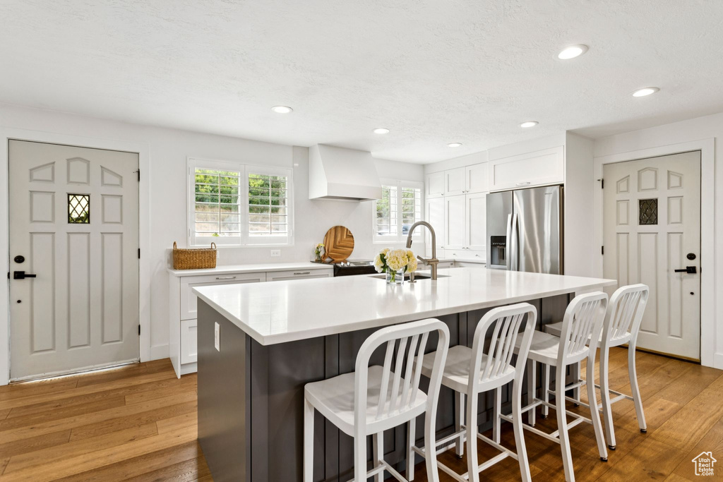 Kitchen featuring stainless steel fridge, a kitchen bar, light wood finished floors, and recessed lighting