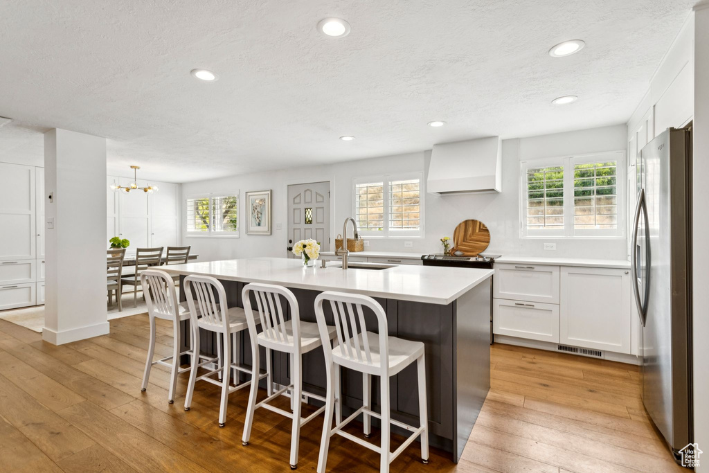 Kitchen featuring freestanding refrigerator, light wood-type flooring, custom range hood, recessed lighting, and a kitchen bar