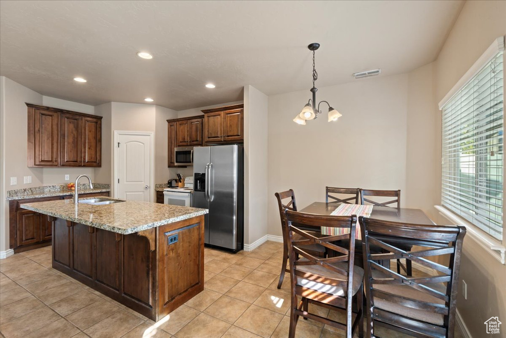 Kitchen with stainless steel appliances, a chandelier, light tile patterned floors, a kitchen island with sink, and decorative light fixtures