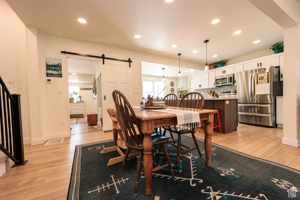 Dining area with light wood-type flooring, a barn door, and recessed lighting