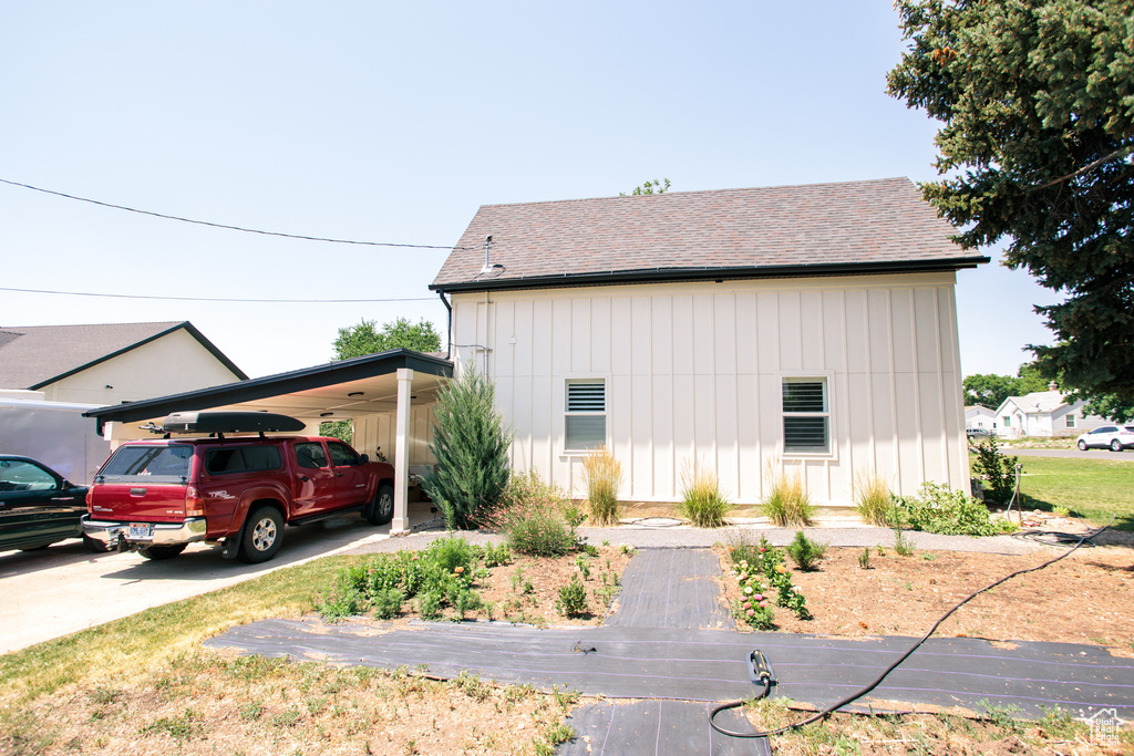 View of side of home featuring board and batten siding, a carport, roof with shingles, and concrete driveway