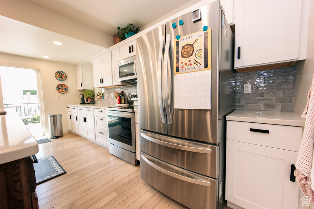 Kitchen with stainless steel appliances, light wood-type flooring, white cabinetry, backsplash, and light countertops