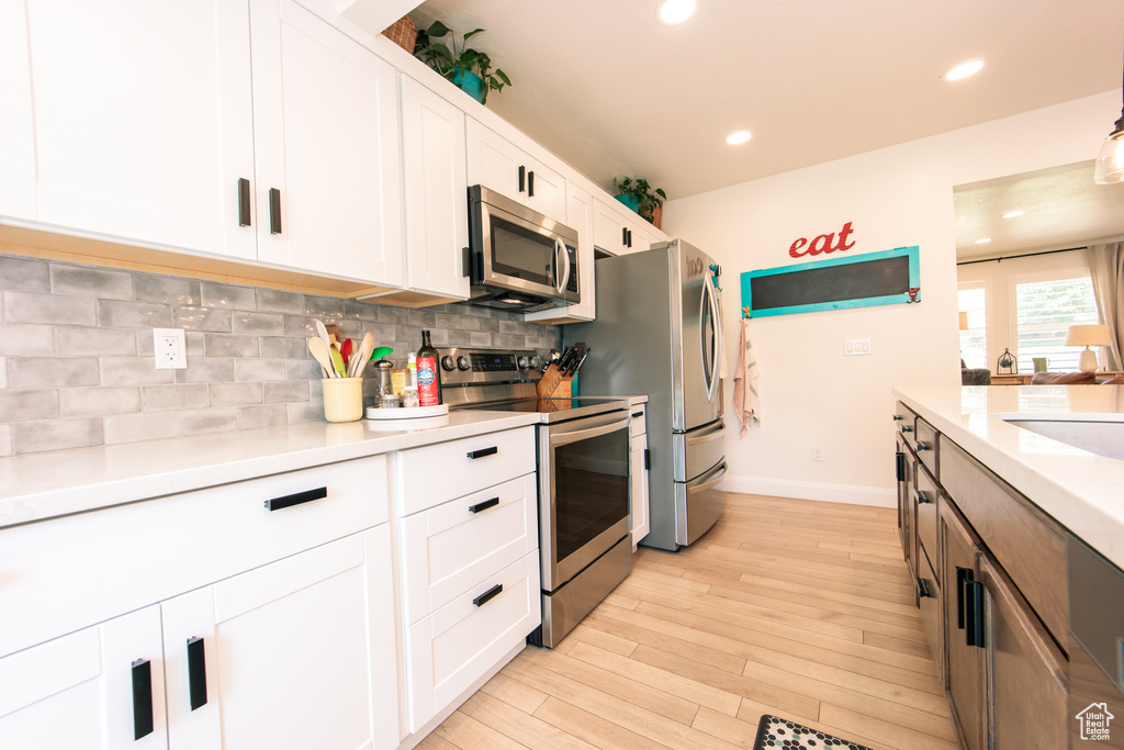 Kitchen featuring appliances with stainless steel finishes, backsplash, white cabinets, light wood-style floors, and light countertops