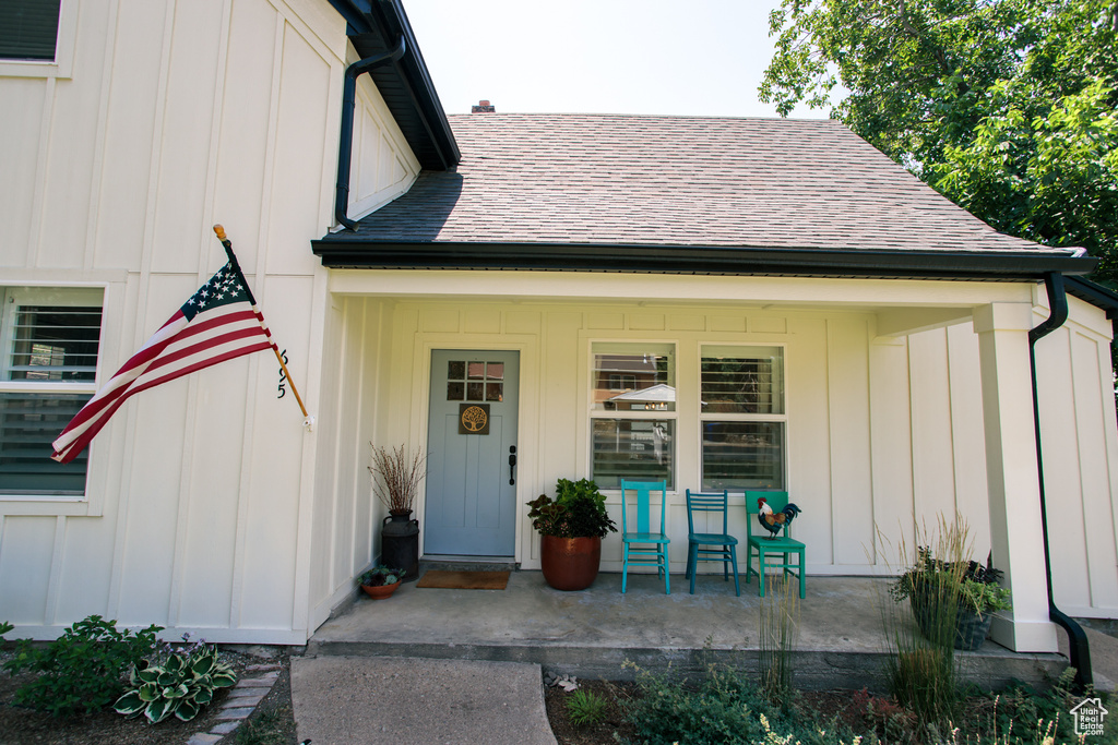 Property entrance with board and batten siding, a porch, and a shingled roof