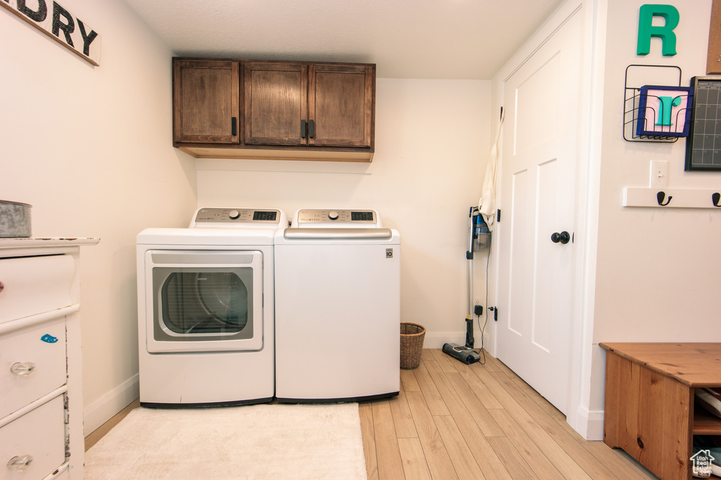 Laundry area featuring washing machine and dryer, light wood-style floors, and cabinet space