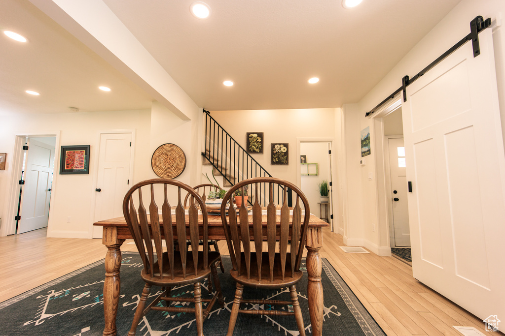 Dining area with a barn door, light wood-style flooring, recessed lighting, and stairs