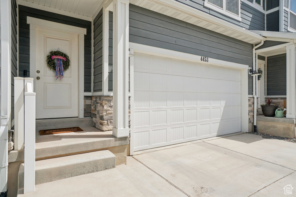 Doorway to property with stone siding, driveway, and an attached garage