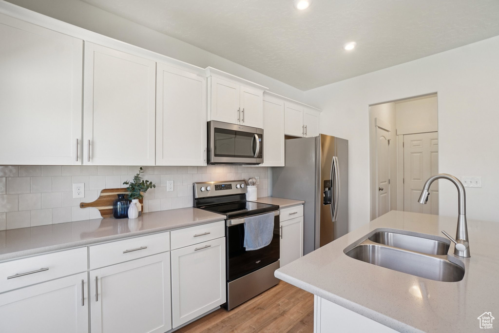Kitchen featuring appliances with stainless steel finishes, light wood-type flooring, backsplash, white cabinets, and recessed lighting