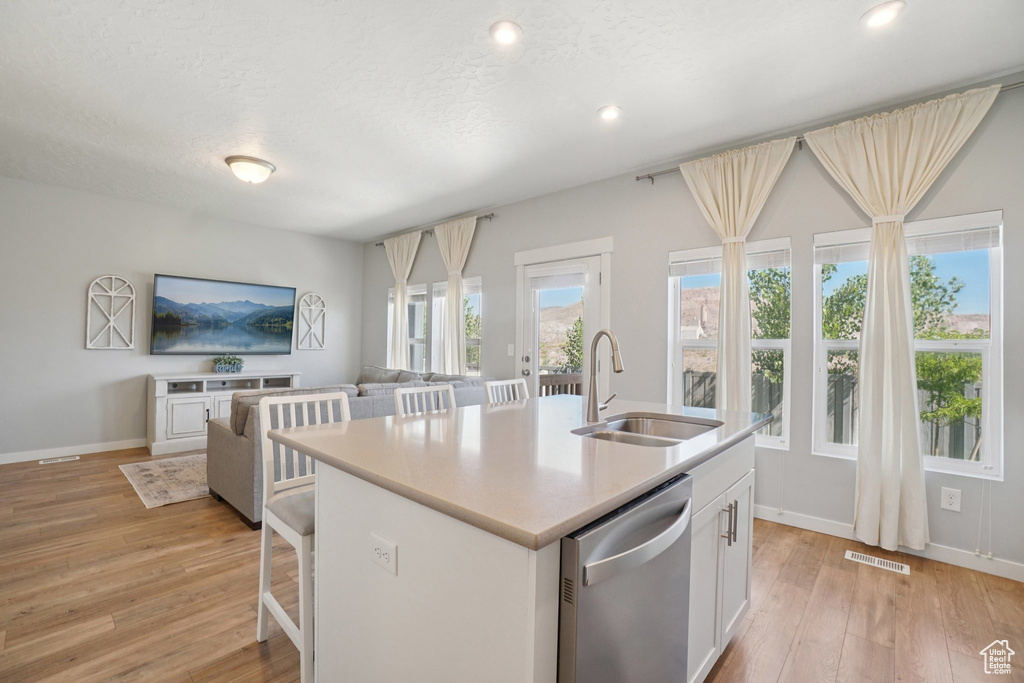 Kitchen with stainless steel dishwasher, open floor plan, light wood finished floors, light countertops, and white cabinetry