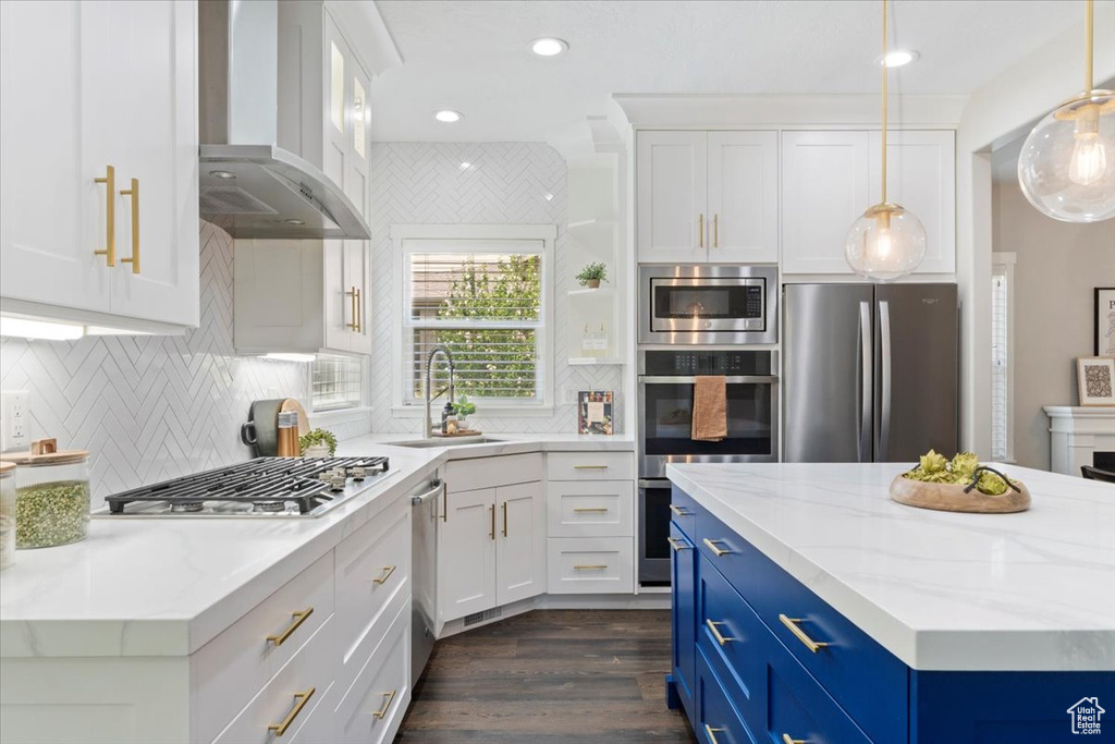 Kitchen featuring blue cabinets, stainless steel appliances, wall chimney exhaust hood, white cabinetry, and dark wood-type flooring