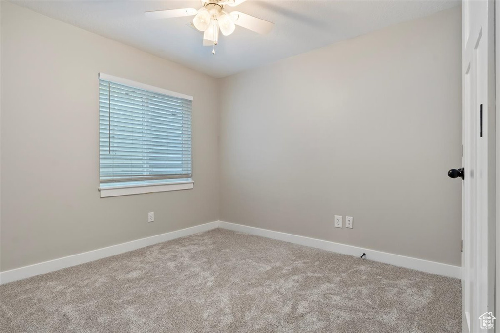 Carpeted spare room with a ceiling fan and baseboards