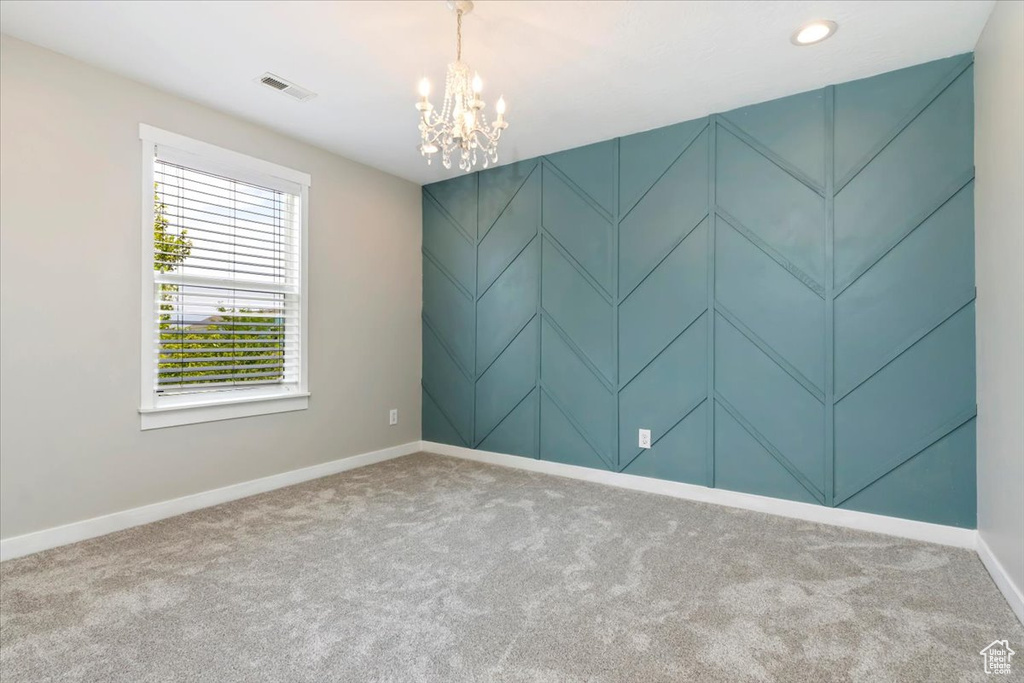 Carpeted spare room featuring a chandelier and baseboards