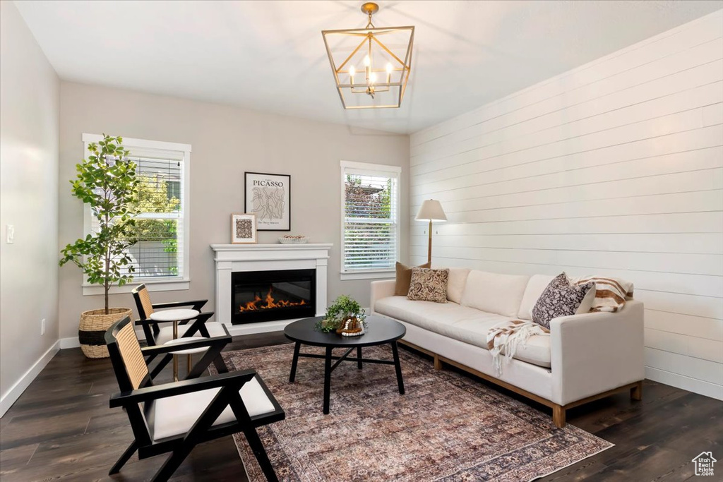 Living room with dark wood-style flooring, a chandelier, a glass covered fireplace, and wooden walls