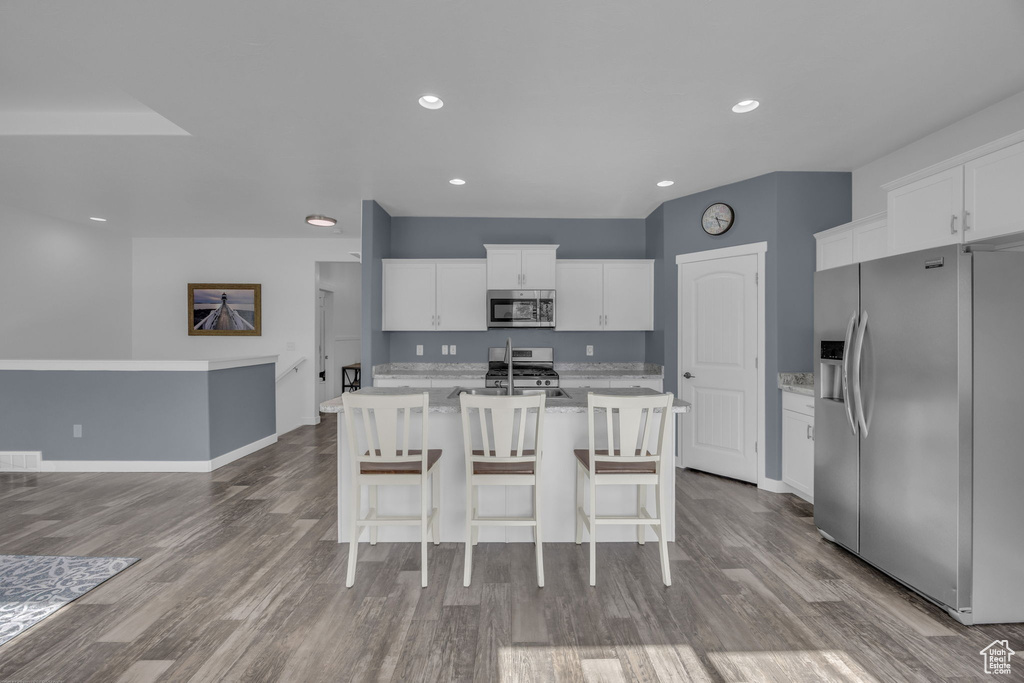 Kitchen with appliances with stainless steel finishes, wood finished floors, recessed lighting, a kitchen island with sink, and a breakfast bar area