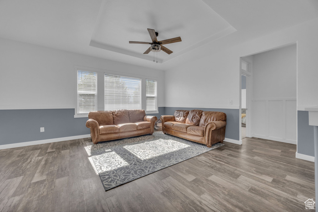 Living room with a tray ceiling, a ceiling fan, and wood finished floors