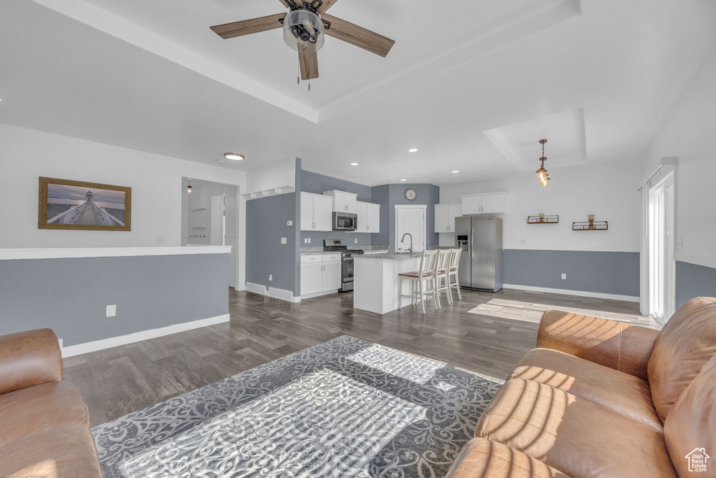 Living area featuring a tray ceiling, ceiling fan, dark wood-type flooring, and recessed lighting